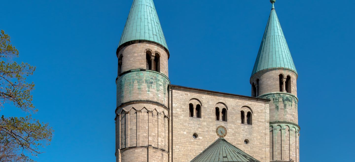 Romanische Stiftskirche St. Cyriakus in Gernrode: zwei runde Westtürme mit grünen Kegeldächern, Rundbogenfenster und heller Sandstein vor tiefblauem Himmel.