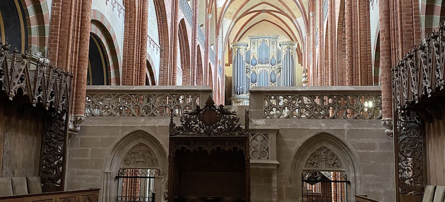 Innenraum des Havelberger Doms: der steinerne Lettner mit Maßwerkbrüstung, dahinter Backsteingewölbe des Mittelschiffs und die Orgel über der Westempore.