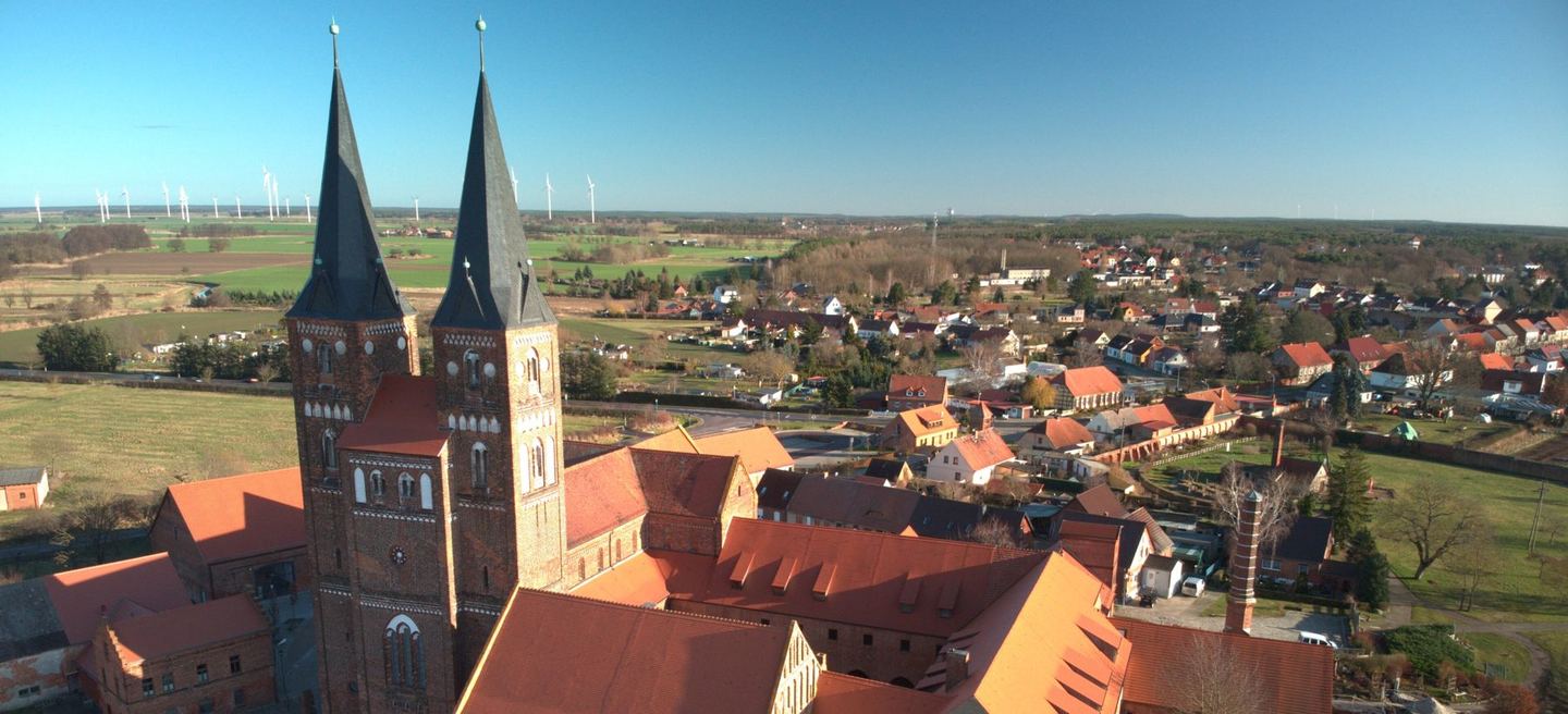 Luftbild des Klosters Jerichow: die romanische Backsteinbasilika mit zwei Westtürmen, die Klostergebäude und das Dorf in der flachen Elbniederung
