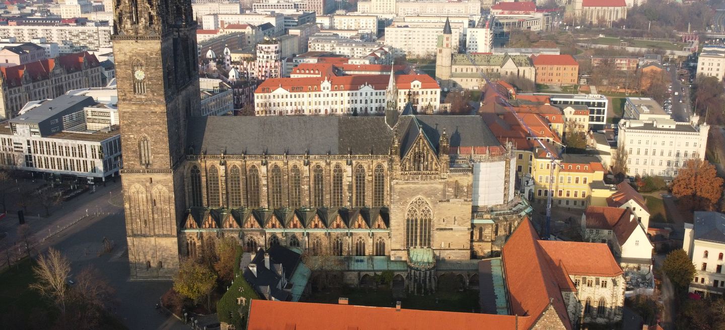 Luftbild des Magdeburger Doms mit Westturm, langem gotischem Langhaus, Strebepfeilern und Kreuzgang, umgeben von der Innenstadt Magdeburgs.