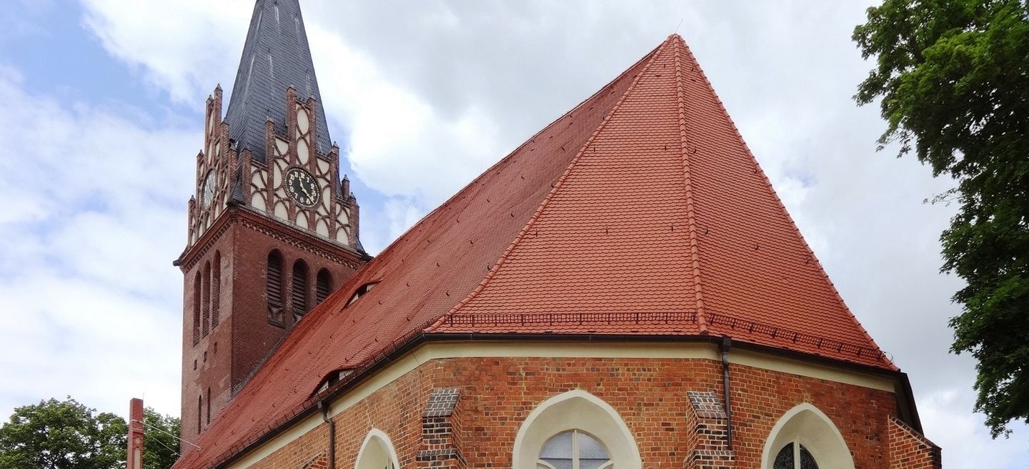 Die Backsteinkirche St. Nikolai in Bad Liebenwerda mit steilem Ziegeldach, spitzbogigen Fenstern und dem Turm mit Uhr und dunklem Helm.