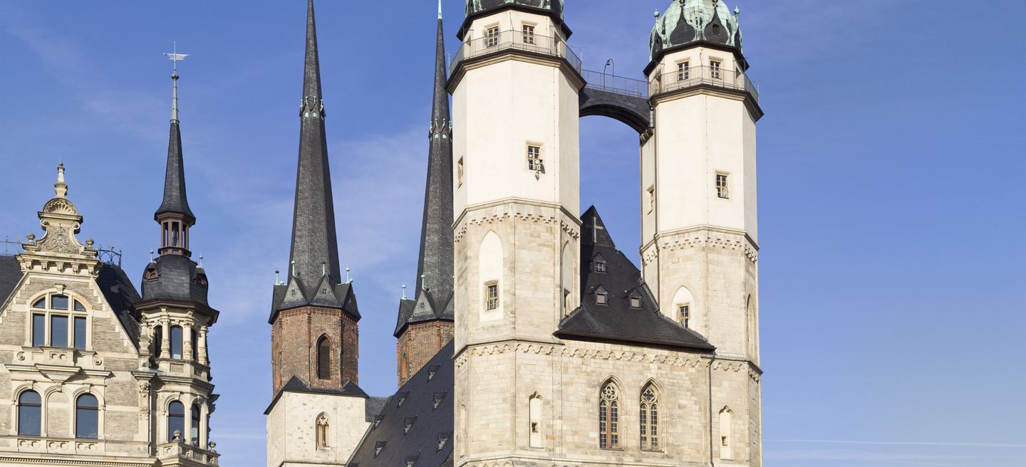Die vier Türme der Marktkirche Unser Lieben Frauen in Halle: zwei helle Hausmannstürme mit Brücke, dahinter die dunklen Blauen Türme.