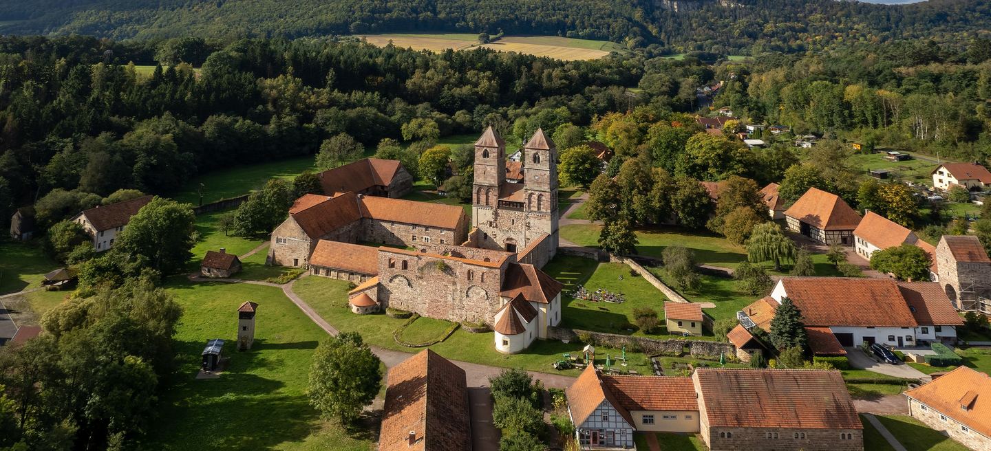 Luftbild des Klosters Veßra im Werratal: romanische Klosterkirche mit zwei Türmen, Fachwerkscheunen des Museumsdorfs, Wiesen und bewaldete Hügel ringsum.