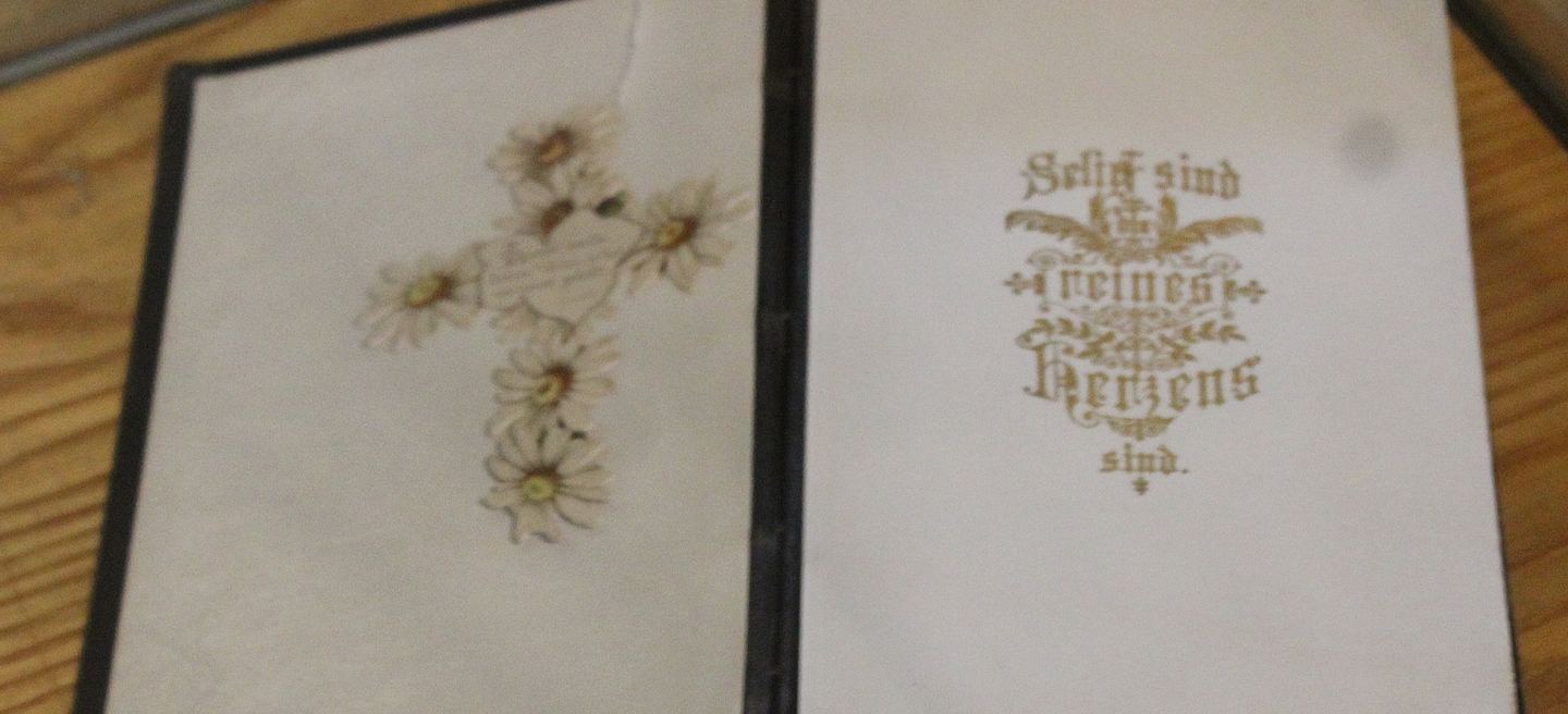 Aufgeschlagenes Gesangbuch von 1887 aus der Kirche St. Pankratius in Rothenschirmbach: rechts die Goldprägung Selig sind, die reines Herzens sind, links getrocknete Margeriten als Kreuz gelegt.
