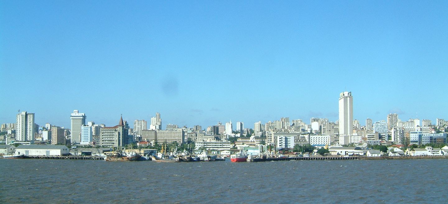 Die Skyline von Maputo vom Wasser aus gesehen, Hochhäuser und Hafenanlagen unter blauem Himmel.