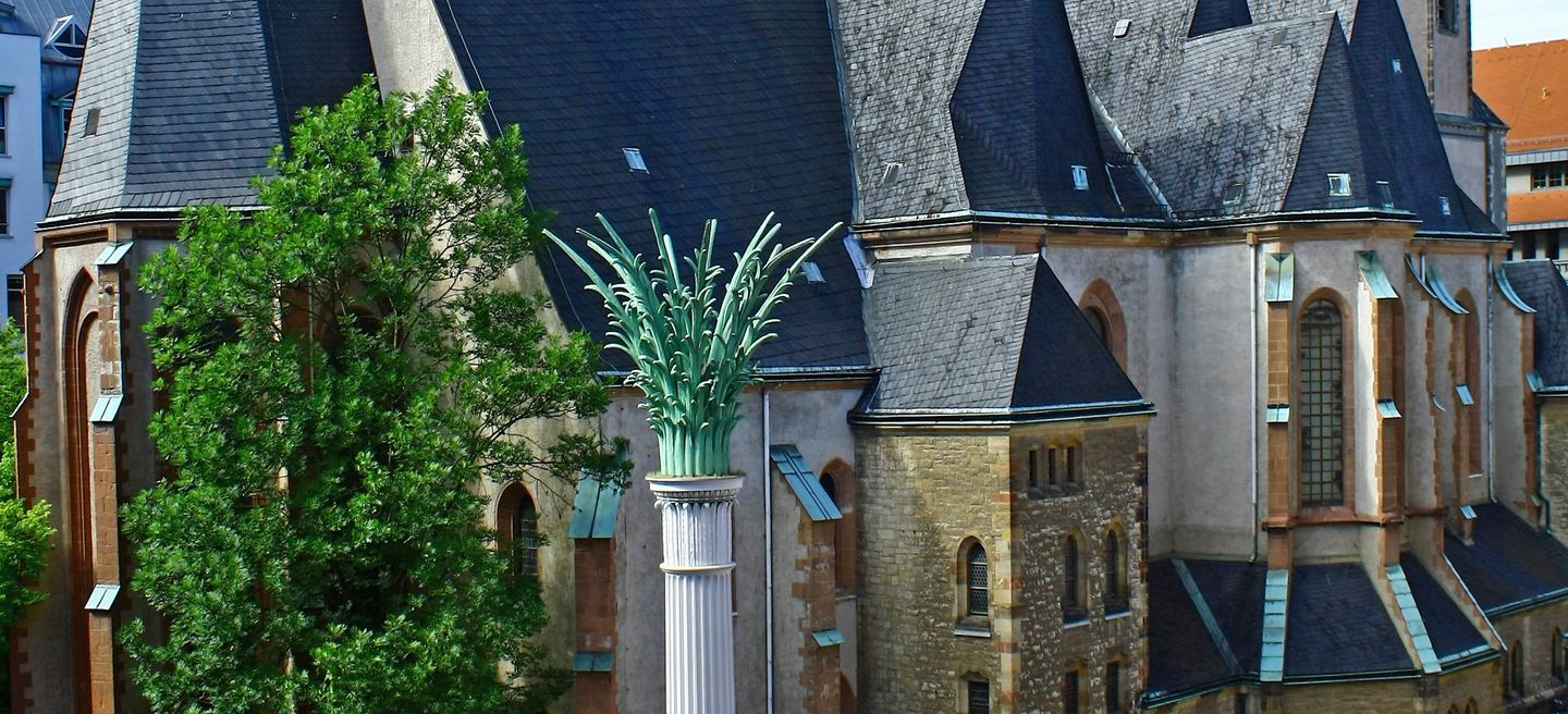 Die Leipziger Nikolaikirche mit steilen Schieferdächern und die Säule auf dem Nikolaikirchhof davor.